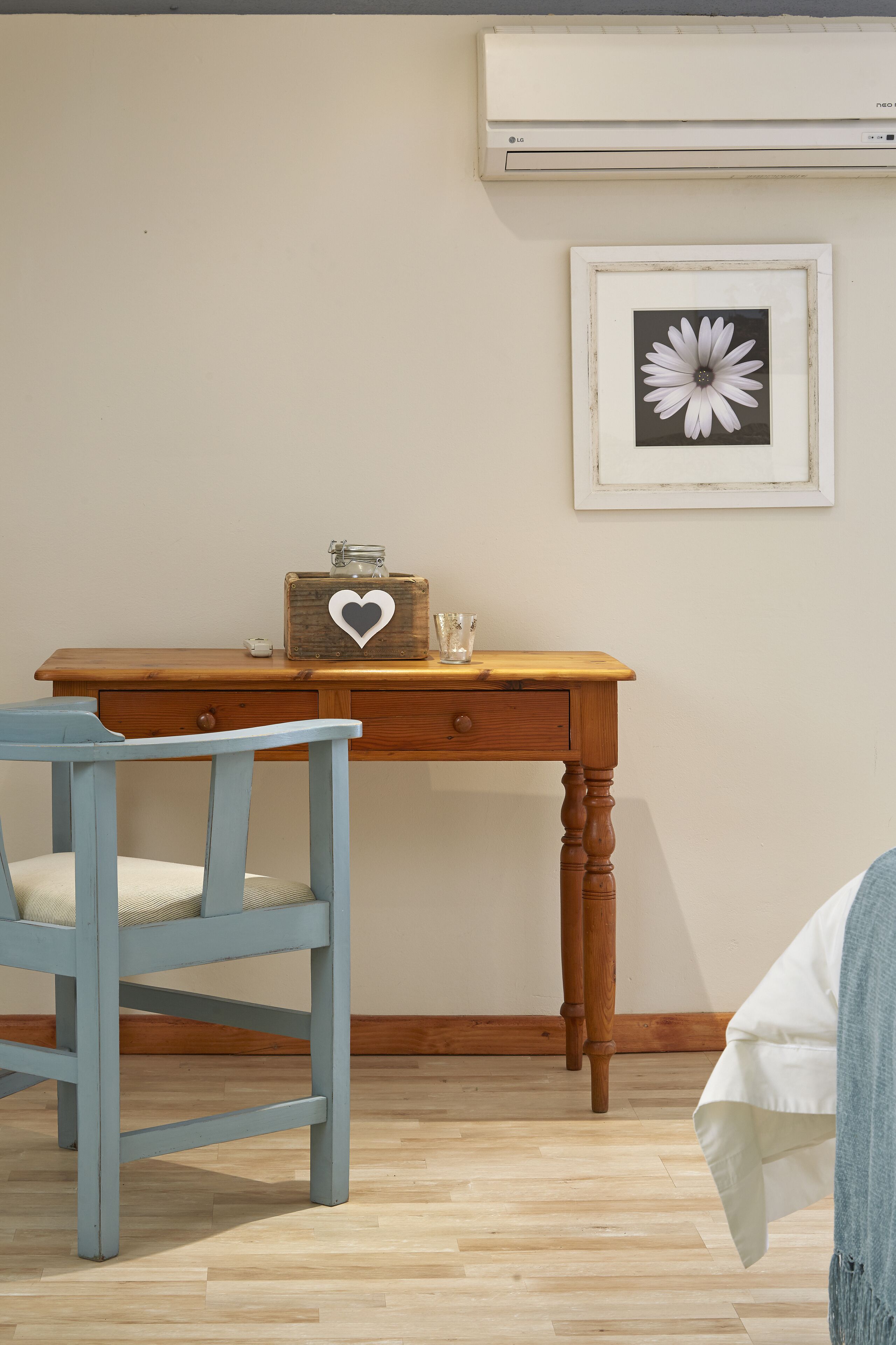 A room with a wooden desk, a chair, a framed picture on the wall, and an air conditioning unit.