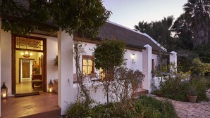 A white building with a thatched roof, a wooden door, and a small window. There is a brick pathway leading to the entrance. - Yellow Aloe Guesthouse (Cederberg)
