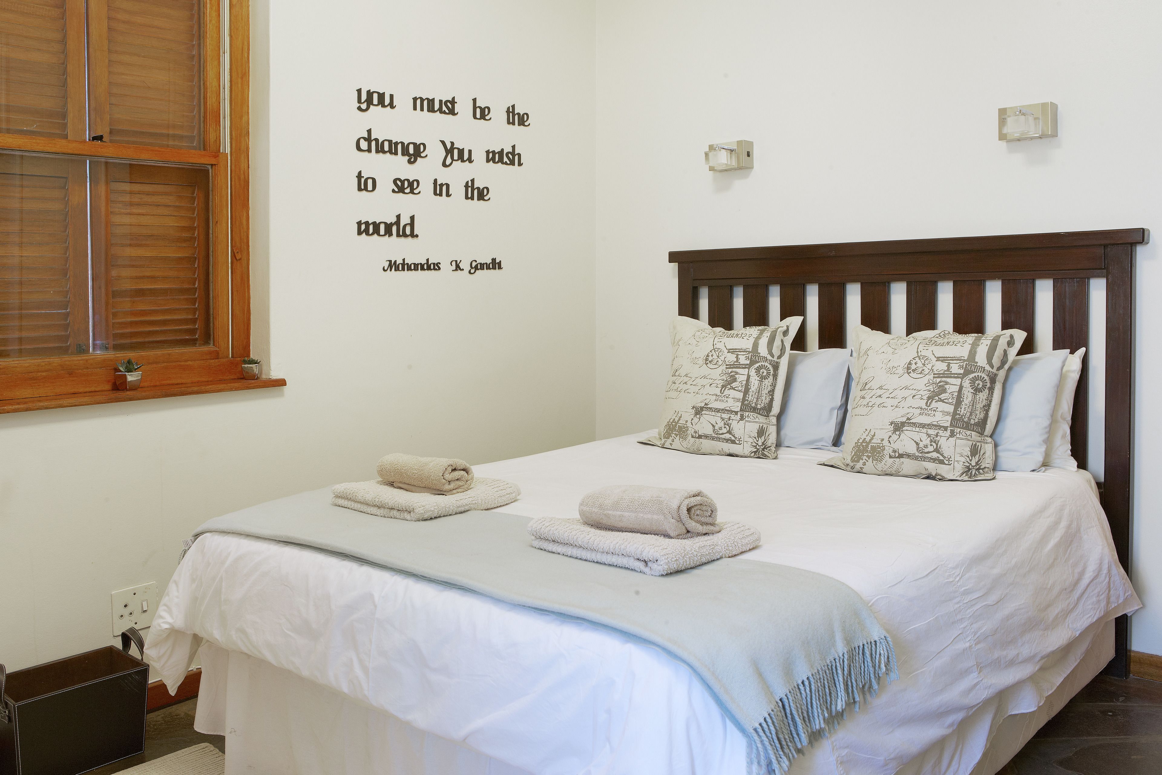 A neatly made bed with white linens and two rolled towels, a wall with a motivational quote, and a wooden headboard.