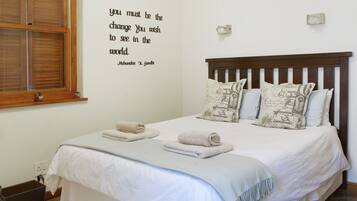 A neatly made bed with white linens and two rolled towels, a wall with a motivational quote, and a wooden headboard.
