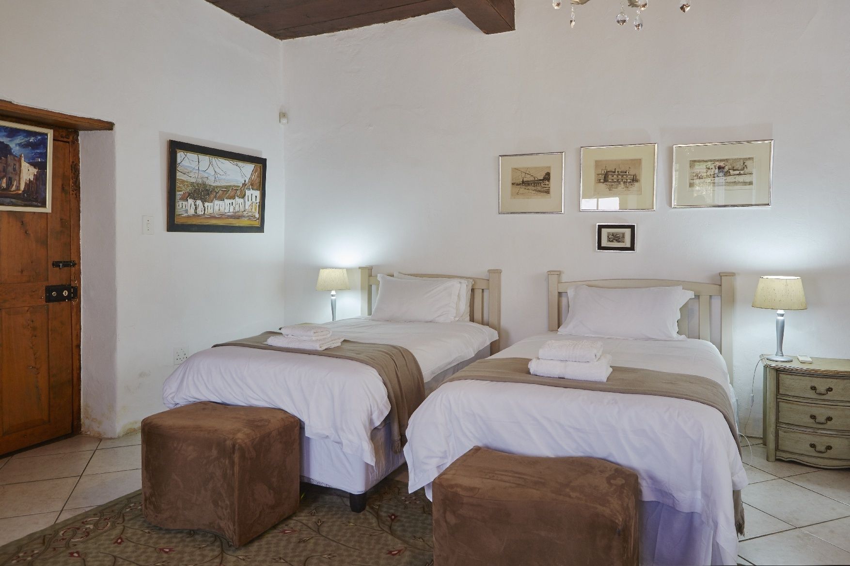 Una habitación con dos camas, una puerta de madera y una mesita con una lámpara.