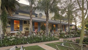 A building with a tiled roof, a satellite dish, and a garden with flowers and sheep statues. - Yellow Aloe Guesthouse (Cederberg)