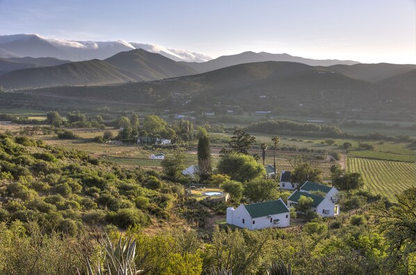 A rural landscape with white houses, a field, and mountains in the background. - Berluda Farmhouse & Cottages (Oudtshoorn)