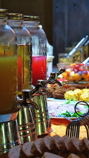 A beverage dispenser with multiple containers, a metal tap, and a buffet table with various food items in the background. - Berluda Farmhouse & Cottages (Oudtshoorn)