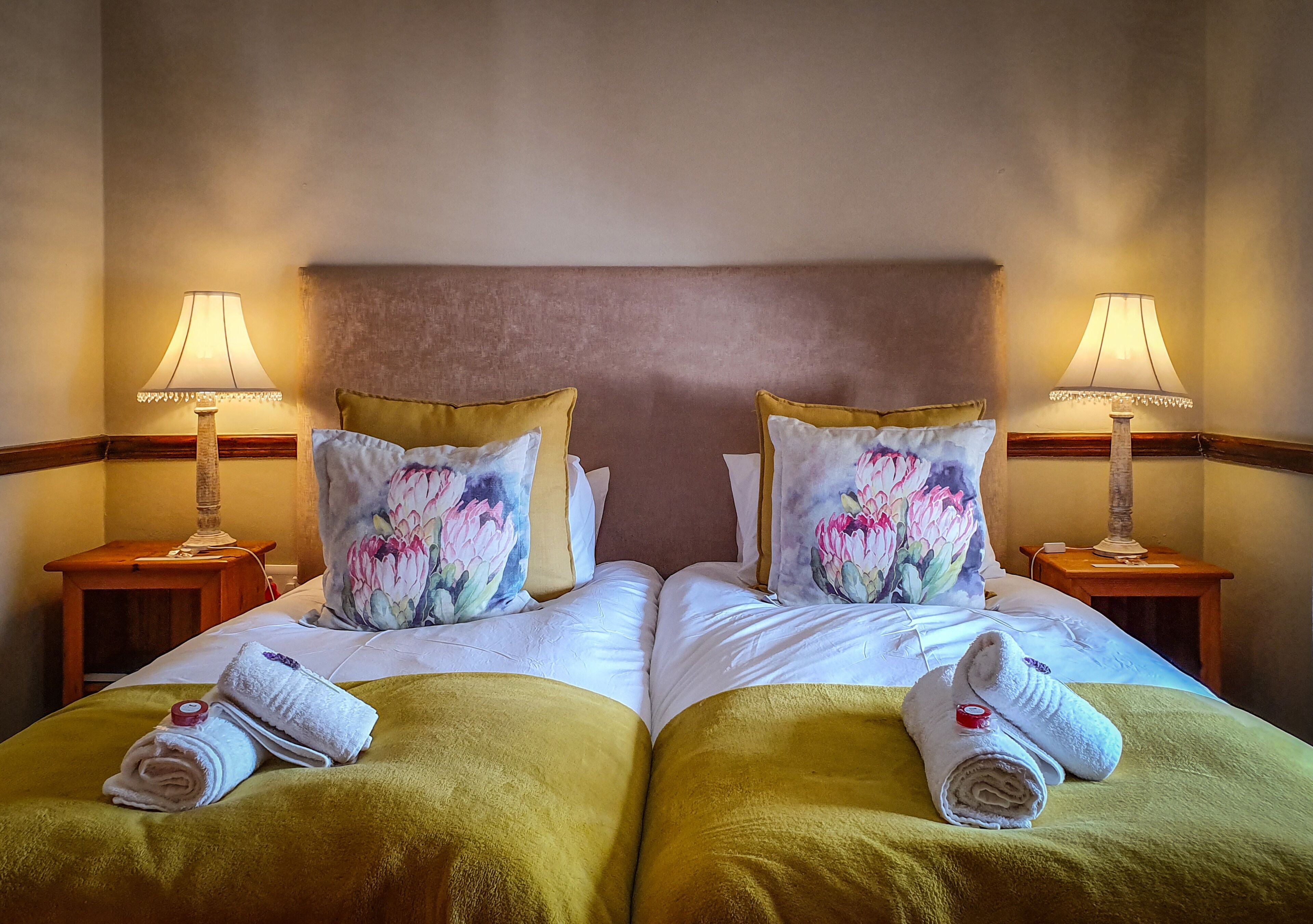 Uma cama de casal com almofadas florais, duas mesas de cabeceira com abajures e toalhas sobre a cama.