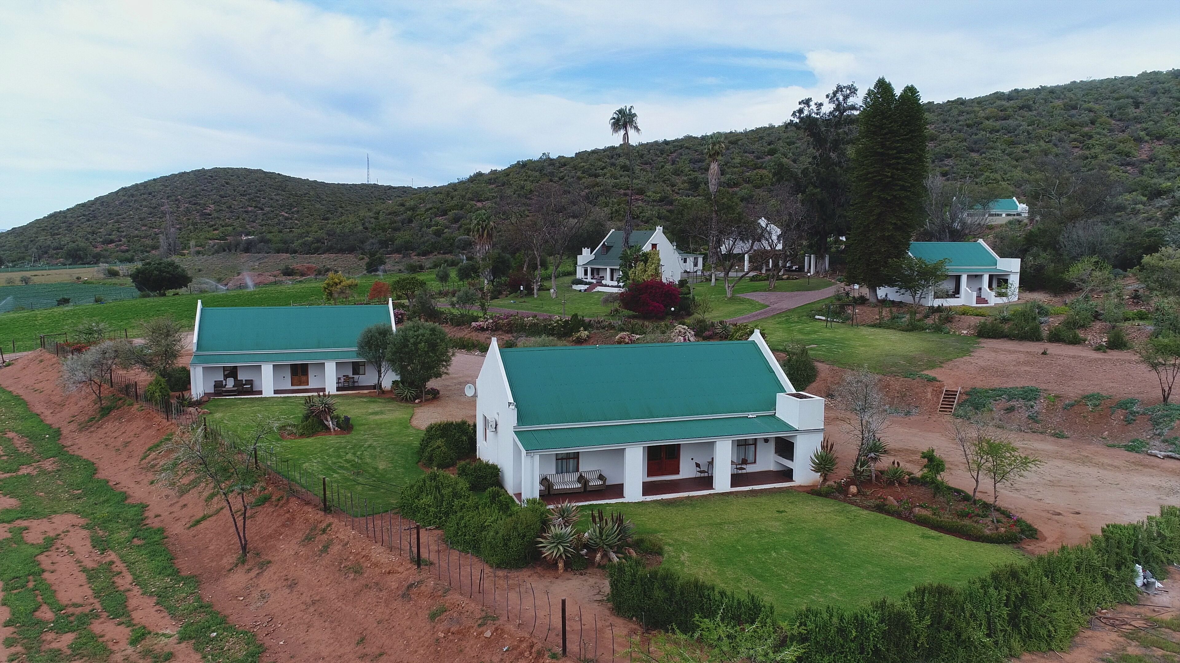A residential area with multiple houses featuring green roofs, surrounded by lush greenery and hills.