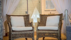 Two wicker chairs with white cushions in a bathroom with a glass shower enclosure and a sink.