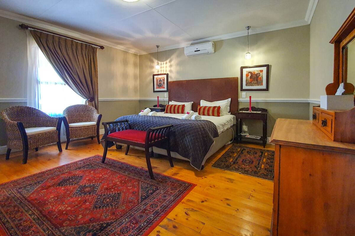 Un dormitorio con dos camas individuales, un tapiz rojo con estampado, sillas de mimbre, una mesita de noche de madera y un espejo.
