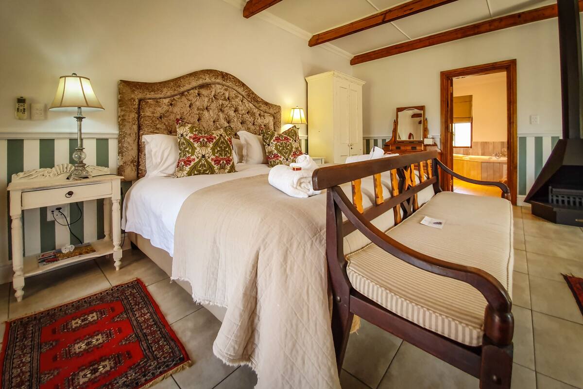 Un dormitorio con una cama grande, una mesita de noche con lámpara, una silla de madera y un tapete rojo.