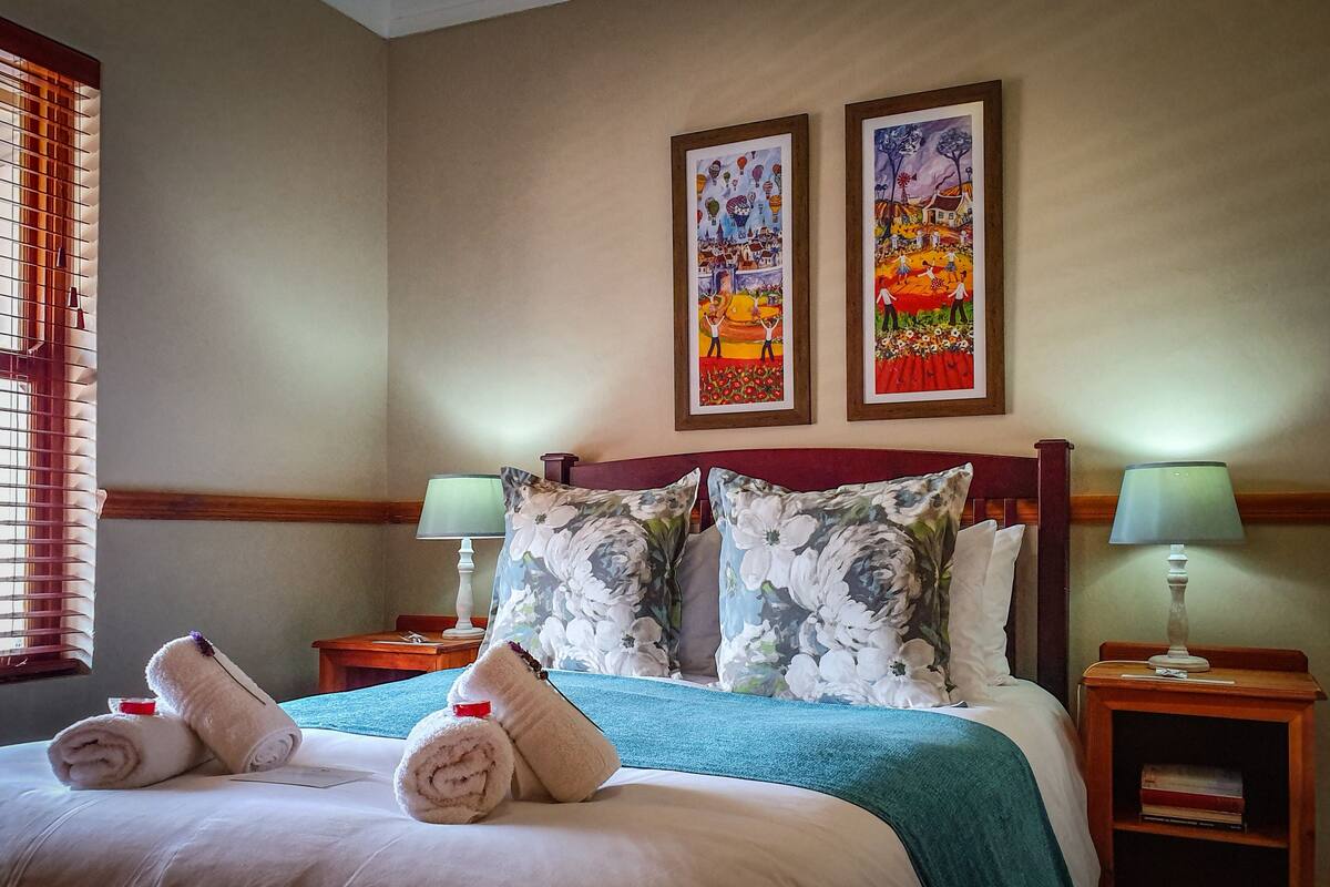 Habitación de hotel con una cama, almohadas estampadas, dos cuadros en la pared y una mesita de noche con una lámpara.