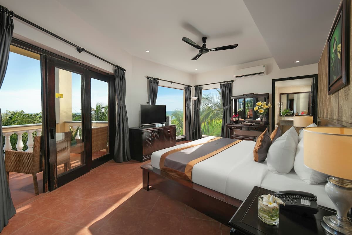 Habitación de hotel con una cama grande, televisión, escritorio con lámpara y balcón con vistas al paisaje.