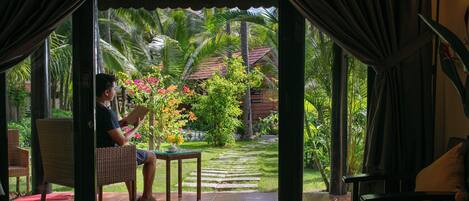 Une pièce avec vue sur un jardin, une personne qui lit et une table avec une chaise.