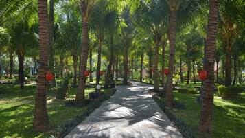A pathway lined with palm trees and red spherical decorations, leading through a lush garden area.