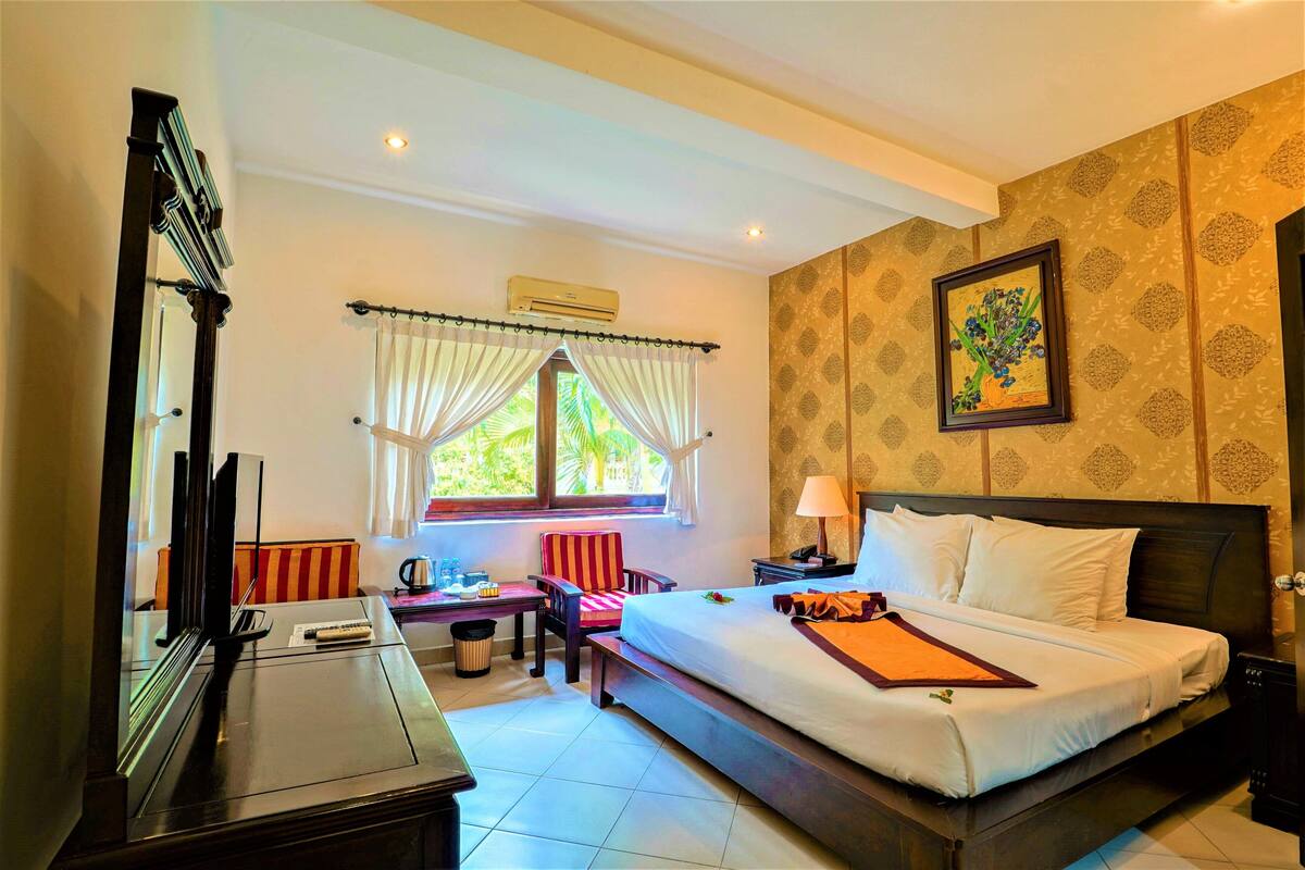 Habitación de hotel con una cama grande, un escritorio con silla, televisión y ventana con cortinas.