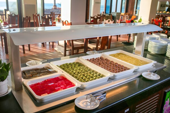 Un bufé con diversos alimentos, incluyendo postres verdes y rojos, y una vista del comedor con sillas y mesas de madera.
