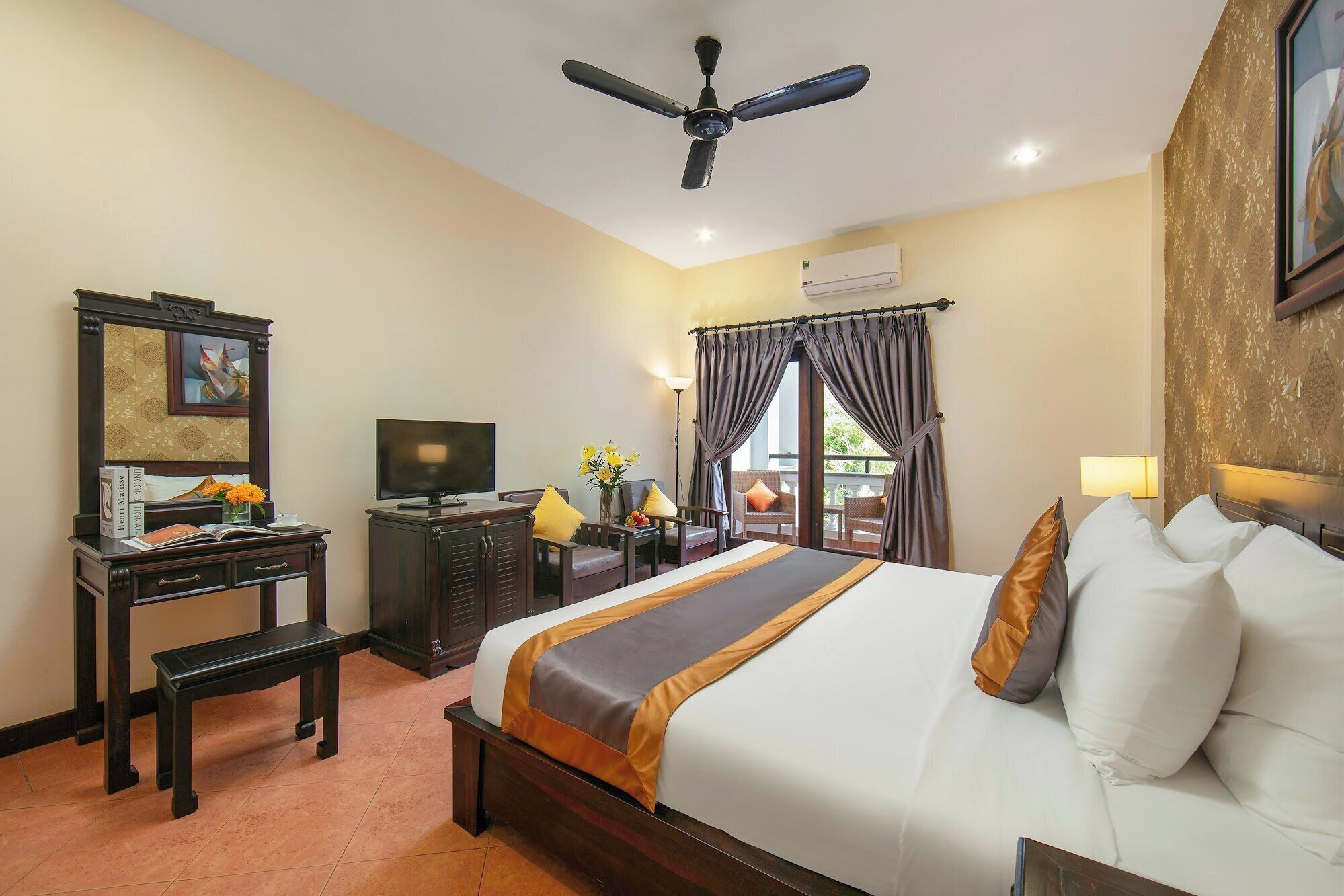 A hotel room with a bed, a desk with a television, a chair, and a window with curtains.