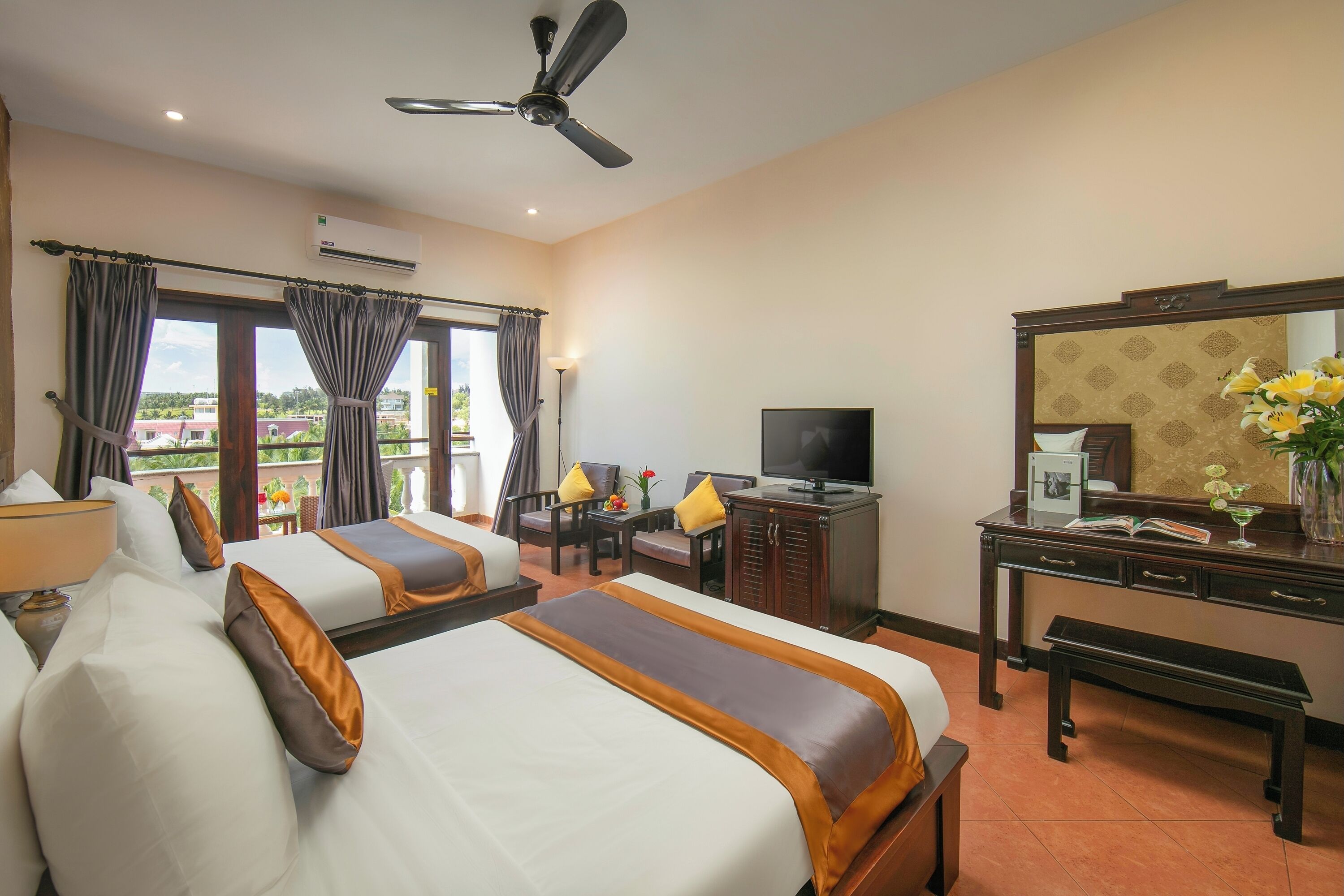 A hotel room with two beds, a desk, a television, and a balcony with curtains.