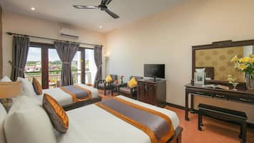 A hotel room with two beds, a desk, a television, and a balcony with curtains.
