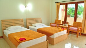 A hotel room with two wooden beds, a small table with chairs, and a view of the garden through the window. - Karon Village Hotel (Karon)
