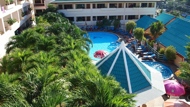 A hotel with a swimming pool, multiple balconies with potted plants, and a view of surrounding buildings. - Karon Village Hotel (Karon)