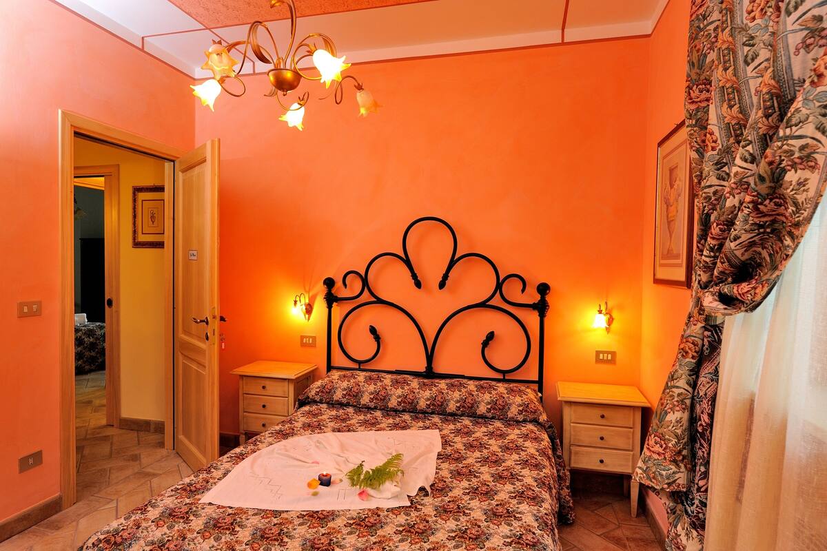 Une chambre à coucher avec une couvre-lit à motifs floraux, une table de chevet avec une lampe et une porte donnant sur une autre pièce.