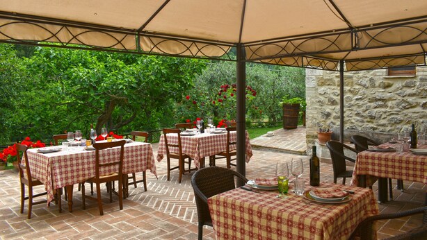 An outdoor patio with tables and chairs, covered by a canopy, and surrounded by greenery and stone walls. - Agriturismo Casa Brunori (Foligno)