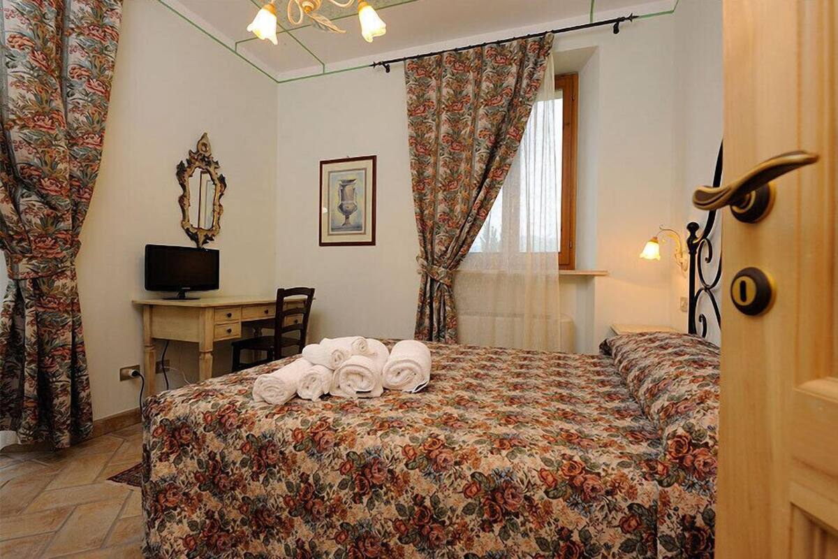 Une chambre à coucher avec une couvre-lit à motifs floraux, un bureau avec une télévision, une chaise et une table de chevet sur laquelle sont pliés des serviettes.