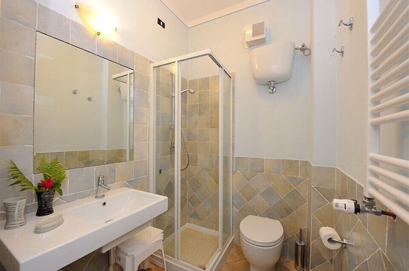 Un baño con ducha de vidrio, lavamanos blanco y retrete.