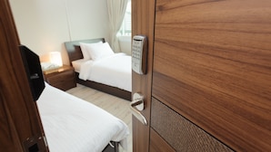 A hotel room with a wooden door, a bed with white linens, a bedside table with a lamp, and a window with curtains. - Big John's Place (Seoul)