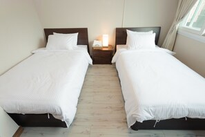 A hotel room with two single beds, a nightstand with a lamp, and a window with curtains.