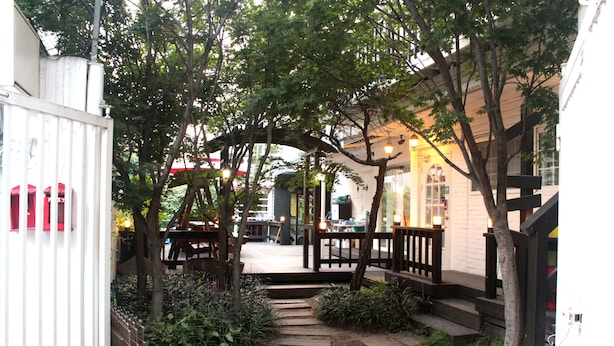 A courtyard with a wooden pathway, surrounded by greenery and a building with a staircase. - Big John's Place (Seoul)