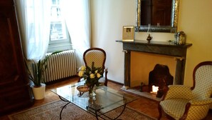 A living room with a glass coffee table, a potted plant, a vase with flowers, a fireplace, and two patterned armchairs. - Antica Dimora B&B in Historic Residence (Bergamo)