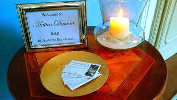 Letrero de bienvenida para Antica Dimora B&B en Residencia Histórica, una vela en un candelabro y una pila de tarjetas de presentación sobre una mesa redonda.