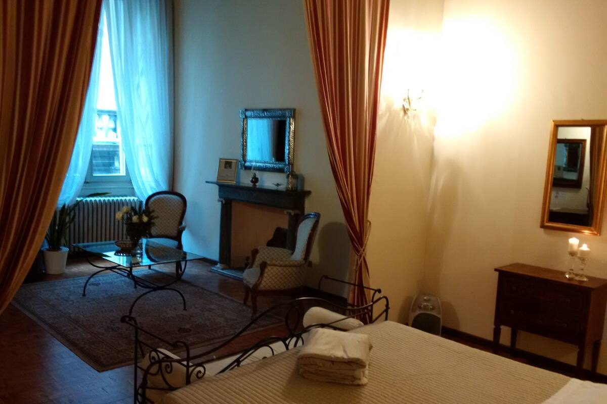 Een slaapkamer met een bed, een stoel, een tafeltje, een spiegel en een open haard.