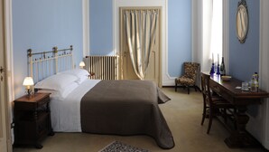 A bedroom with a large bed, a chair, a table, and a chandelier. - Antica Dimora B&B in Historic Residence (Bergamo)