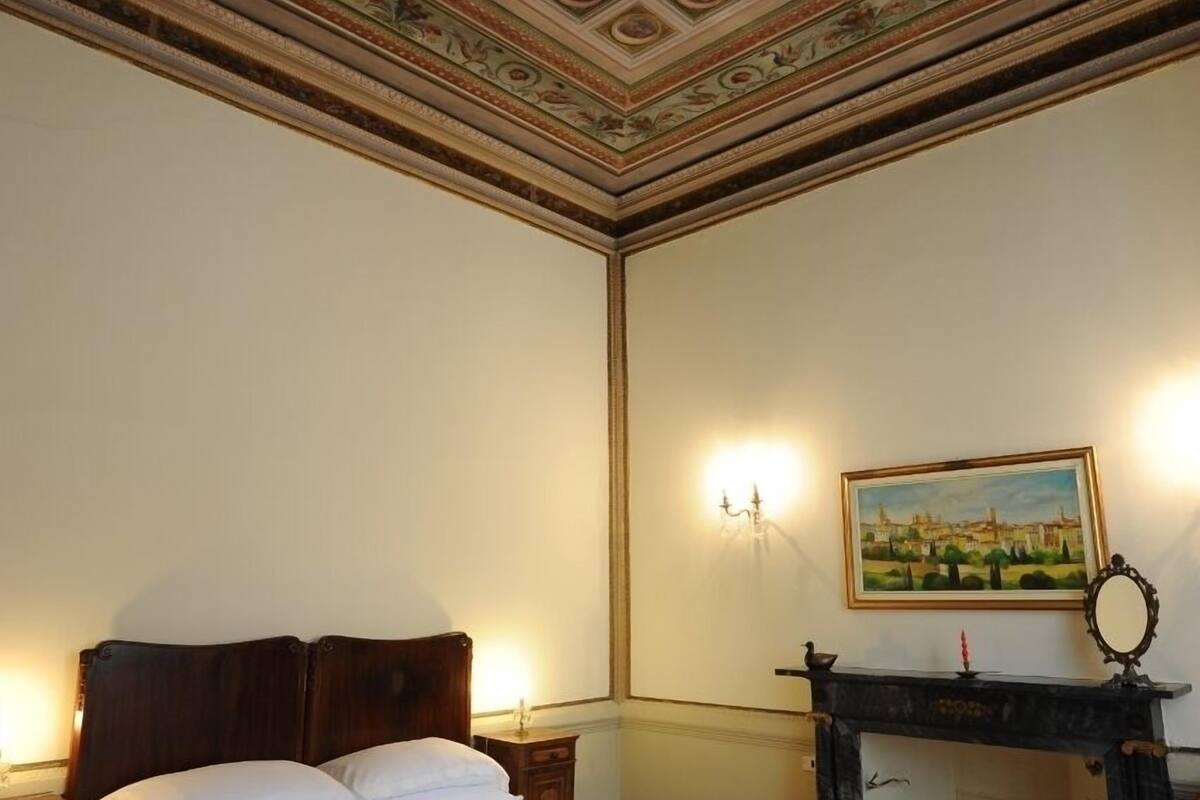 Een slaapkamer met een groot bed, een open haard, een schilderij aan de muur en een gedetailleerd plafond.