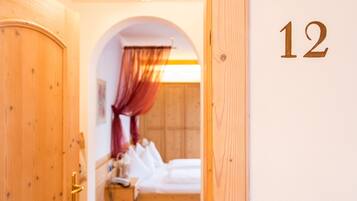 Ein Hotelzimmer mit Holztür, der Wand ist die Nummer 12 angebracht, ein Bett mit weißer Bettwäsche und ein Nachttisch mit Lampe.
