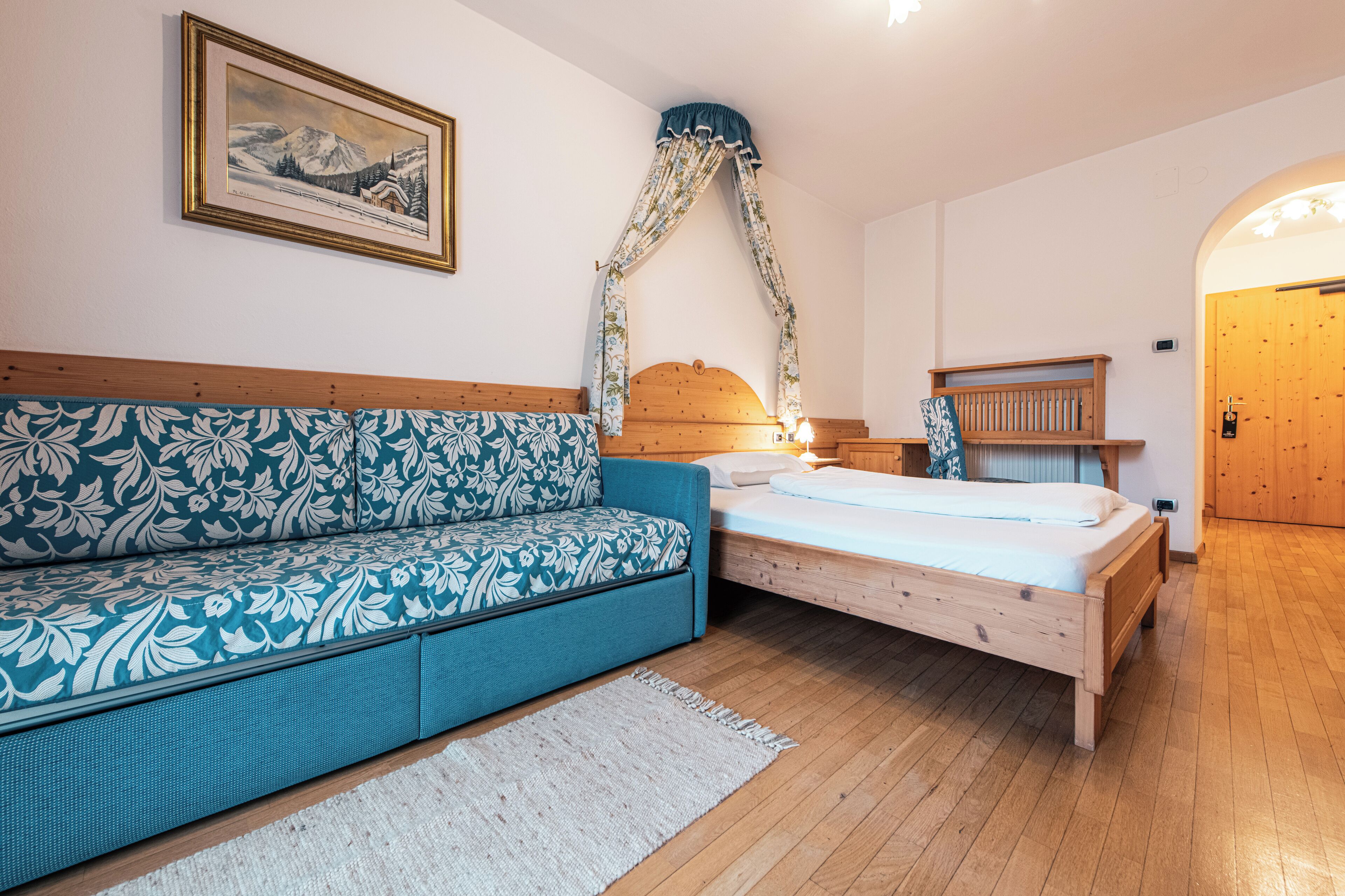 Une chambre à coucher avec un lit, un canapé, une tête de lit en bois, un tableau accroché au mur et une porte en bois.