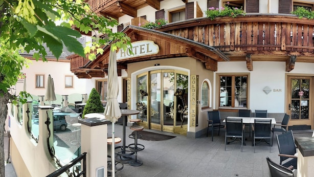 A hotel with a wooden balcony, outdoor seating area, and a sign reading "HOTEL". - Hotel Goldene Rose (Monguelfo)