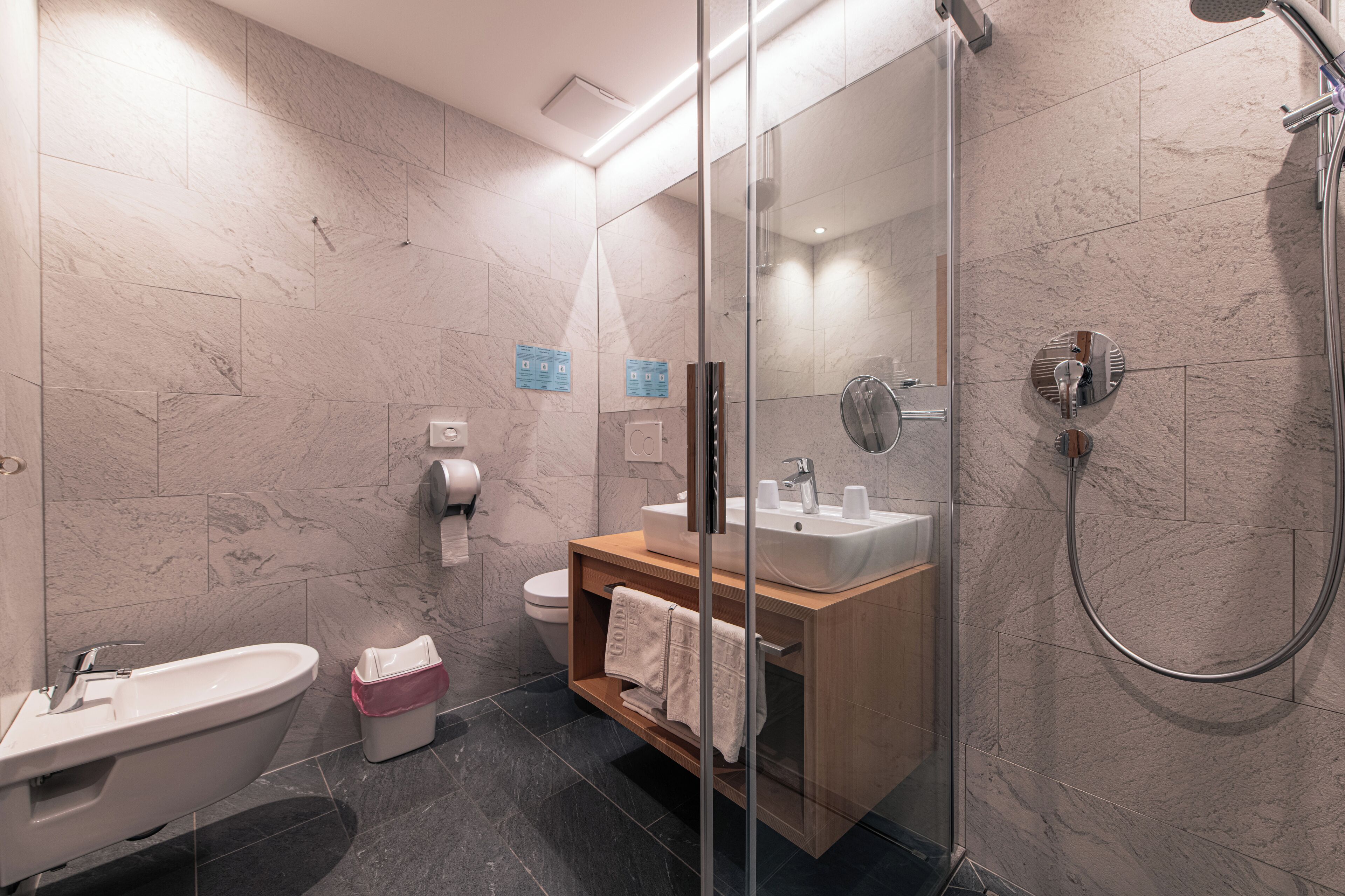 Une salle de bain moderne avec une douche à parois de verre, un meuble-lavabo en bois, un lavabo blanc et des toilettes.