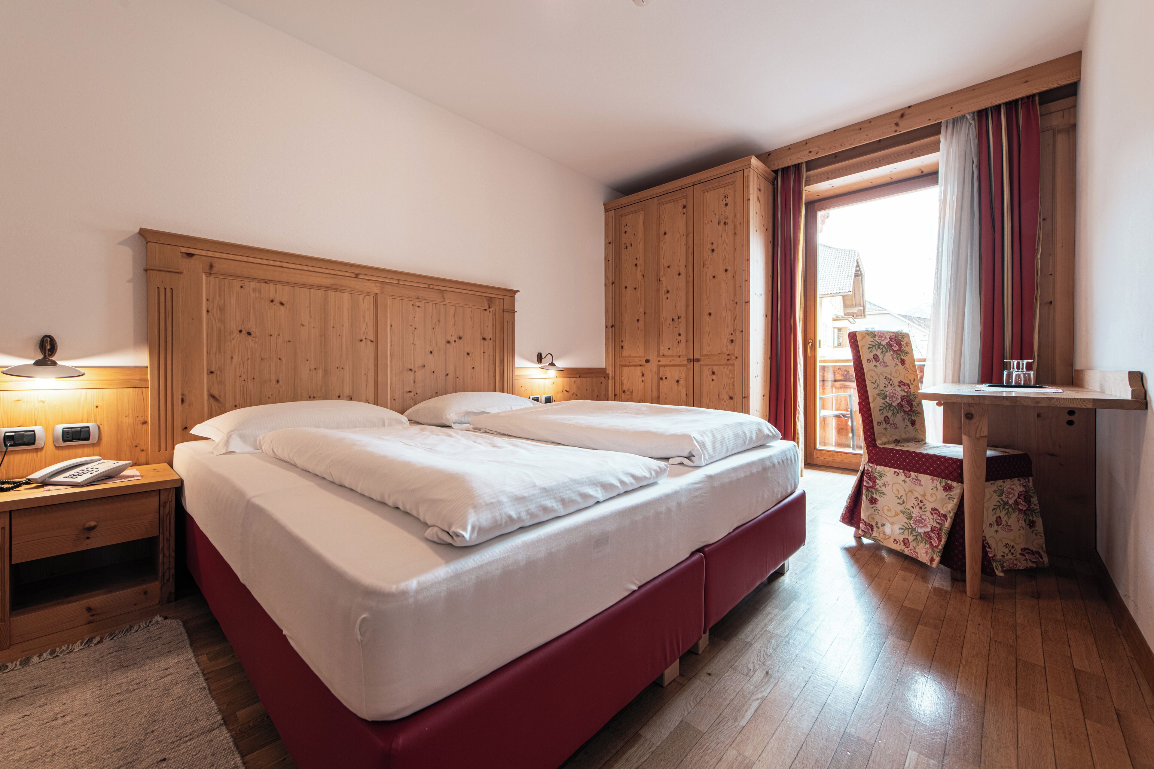 Habitación de hotel con dos camas, armario de madera, escritorio, silla y ventana con cortinas.