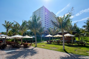A hotel courtyard with outdoor seating, palm trees, and a building in the background. - Dessole Beach Resort Nha Trang (Cam Lam)