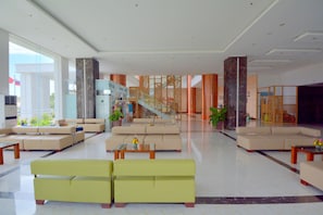 En rummelig lobby med flere siddeområder, en trappe og en reception.