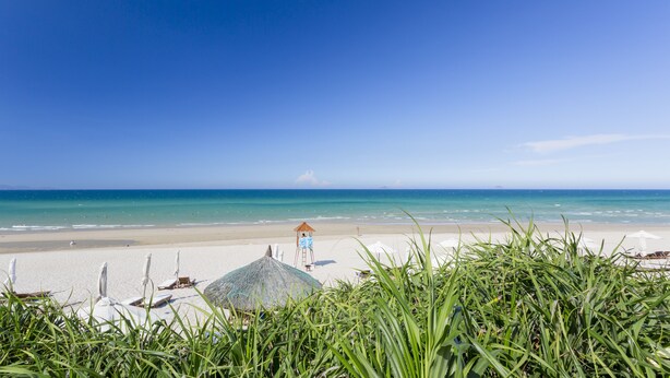 A beach with a clear sky, a lifeguard tower, and umbrellas. - Dessole Beach Resort Nha Trang (Cam Lam)