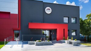 A modern building with a red and grey facade, a prominent 'Automobil Hotel' sign, and a well-maintained entrance area with planters and a bench. - Automobil Hotel (Kraków)