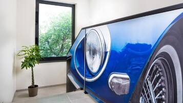 Un coche azul estacionado dentro de una habitación con una planta en maceta y una ventana.