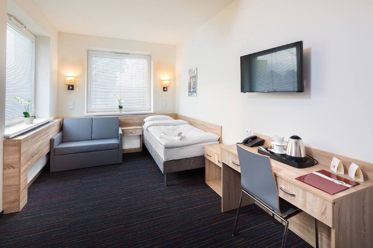 Una habitación de hotel compacta con cama, escritorio, silla, sofá pequeño y televisor.