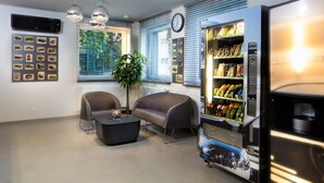 A modern living room with two sofas, a coffee table, a potted plant, a wall-mounted clock, and a vending machine. - Automobil Hotel (Kraków)