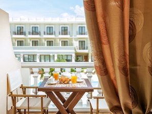 Un balcón con una mesa dispuesta para el desayuno, que incluye cruasanes, jugo y café.