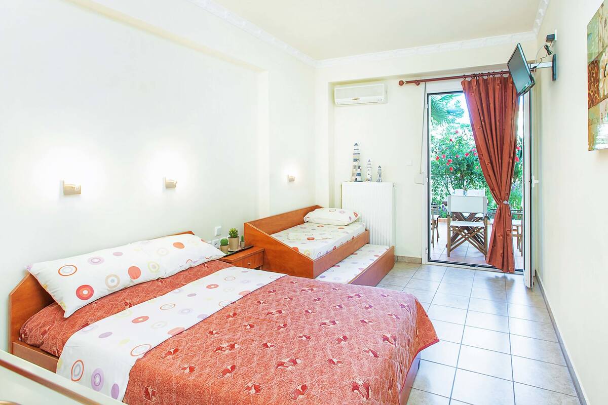 Habitación de hotel con dos camas, una mesita pequeña y vistas al exterior a través de una puerta corrediza.